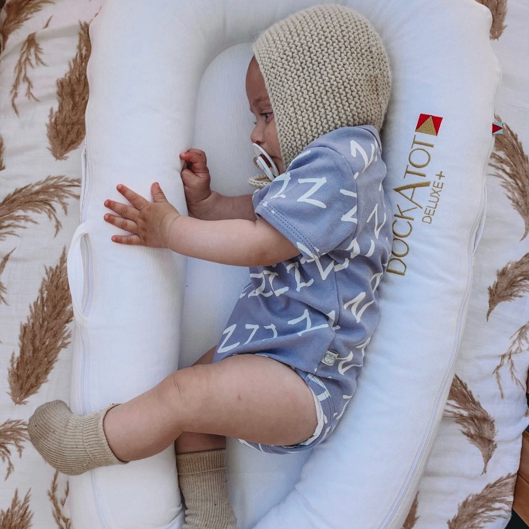 Kippins Bam short sleeve bodysuit for babies, light fabric with snap closures, in a soft, neutral color.
