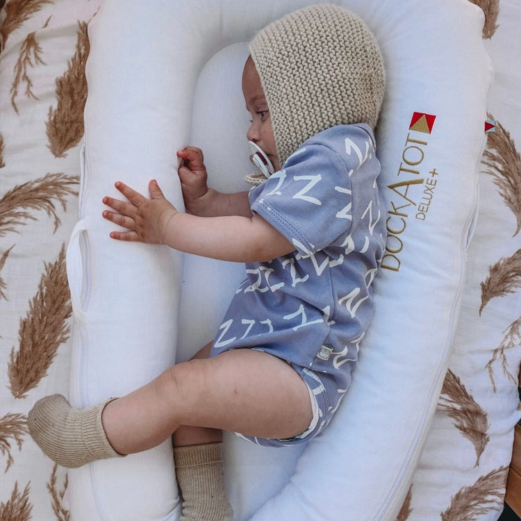 Kippins Bam short sleeve bodysuit for babies, light fabric with snap closures, in a soft, neutral color.